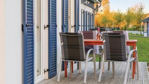 A wooden deck with outdoor furniture, including chairs and a table, and a building with blue shutters. - Ferienhaus 2 Altefähr (Altefähr/Rügen)