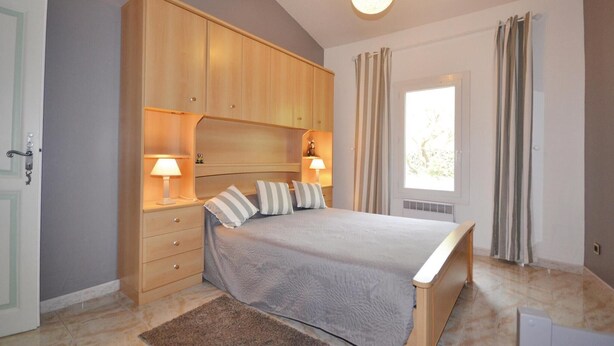 Een slaapkamer met een bed, nachtlampjes, een houten garderobe en een raam met gordijnen.