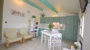 Een compacte keuken met groene kastjes, een eettafel met stoelen, en een klein zithoekje met twee fauteuils.