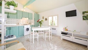 Een keuken met blauwgroene kastjes, een witte tafel en een televisie aan de muur.