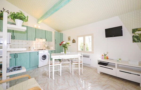 A kitchen with teal cabinets, a white table, and a TV mounted on the wall.