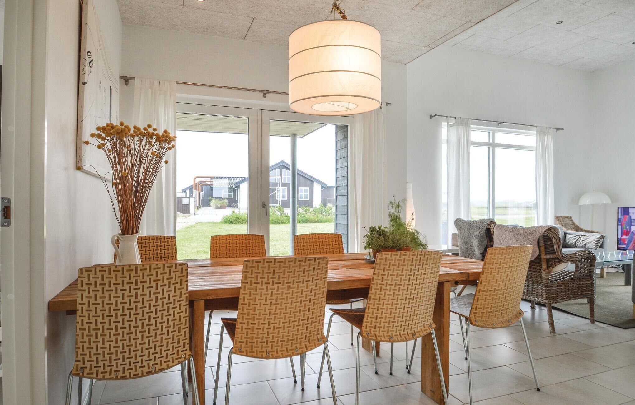 A dining area with a wooden table and wicker chairs, a hanging light fixture, and a view of a house through glass doors.