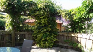 Un patio con una mesa redonda y sillas, rodeado por una valla de madera y abundante vegetación.