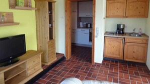 Cocina compacta con armarios de madera, una cafetera y un televisor sobre un mueble de madera.