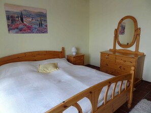 A bedroom with a wooden bed, a wooden dresser with a mirror, and a nightstand with a lamp. - Heidelberg, 2 BR, EC, 52m² - Heidelberg, Viola (Neustadt in Holstein)