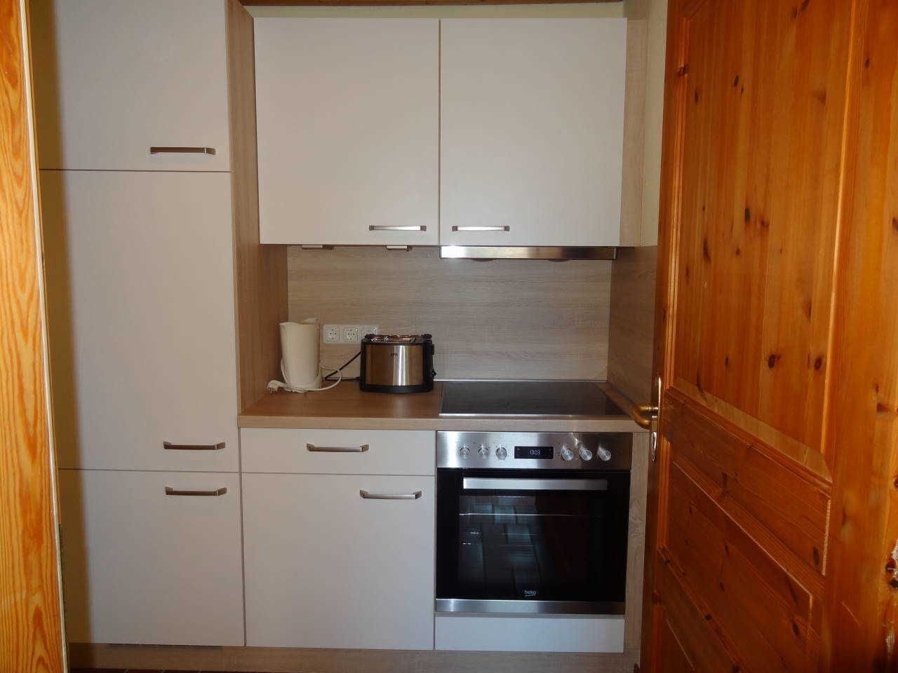 Eine kleine Küche mit weißen Schränken, einem Edelstahlbackofen und einer Holztür.