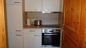 Una cocina compacta con armarios blancos, horno de acero inoxidable y puerta de madera.