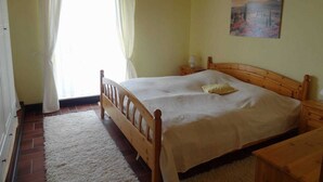 Un dormitorio con cama de madera, mesita de noche, un cuadro en la pared y ventana con cortinas.