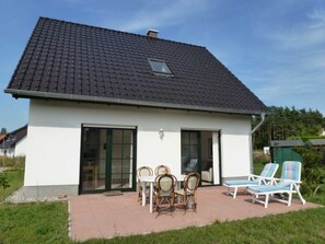 A two-story house with a tiled roof, a patio with outdoor furniture, and a green garden.