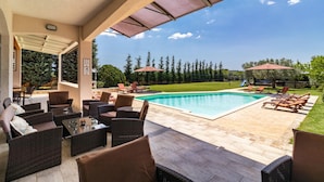 Une terrasse extérieure aménagée avec des meubles en osier, une piscine et un espace abrité avec des parasols.