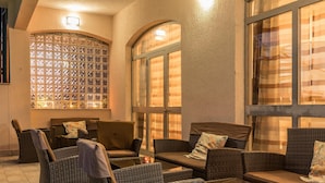 Un coin salon accueillant, avec des meubles en osier et un mur décoratif composé d’une grille de panneaux de verre.