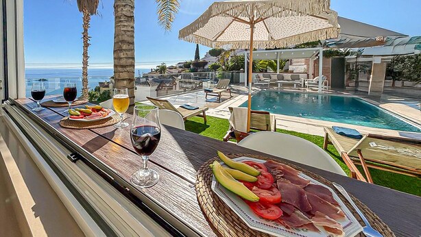 A balcony with a view of a pool, dining table with food and drinks, and a tropical setting. - Nice home in Almuñecar (Almuñecar)