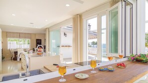 A modern kitchen with a central island, a dining area with chairs, and a view of the outdoors through large windows. - Nice home in Almuñecar (Almuñecar)