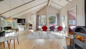 Een knus vakantiehuisje met houten inrichting, een eethoek met rode stoelen, een televisie en een houtkachel.