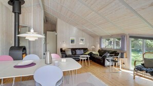 Een ruime woonkamer met een hoge plafond, een open haard, een eettafel met stoelen, een bank en een raam met uitzicht op de omgeving.
