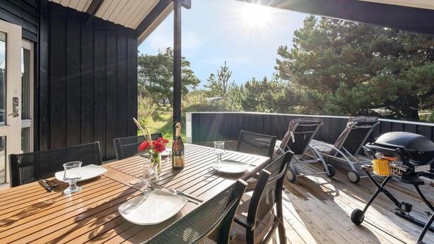 Een eethoek buiten met een houten tafel, stoelen en een barbecue.