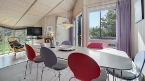 Een moderne eetruimte met een lange tafel, rode en grijze stoelen, een televisie en uitzicht op de omgeving.