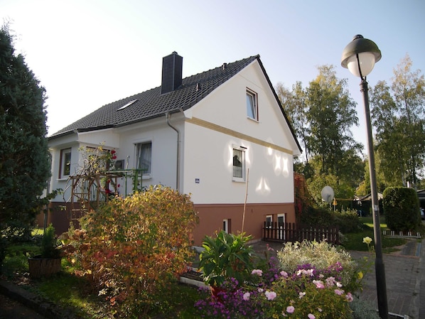 A two-story house with a sloped roof, a visible chimney, and a small porch with a chair.