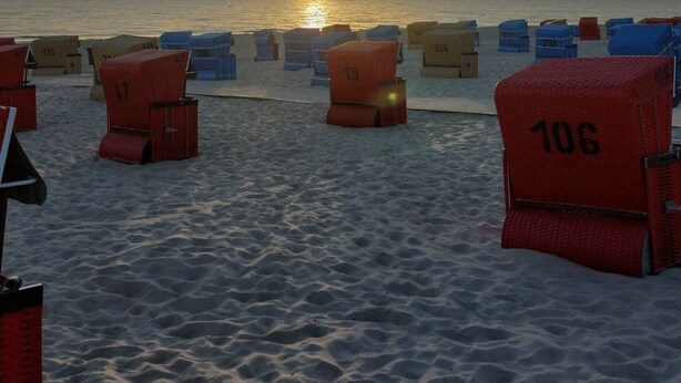 Una playa con sillas de playa numeradas y una puesta de sol al fondo.