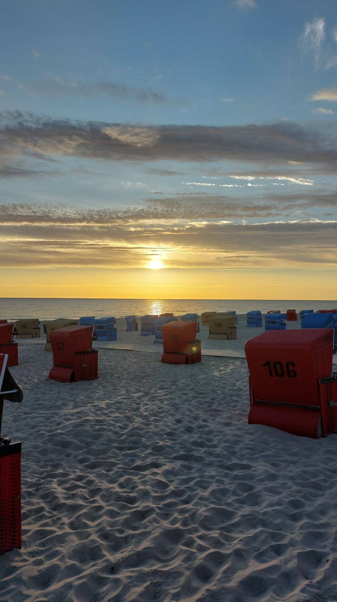 Een strand met genummerde ligbedden en een ondergaande zon.
