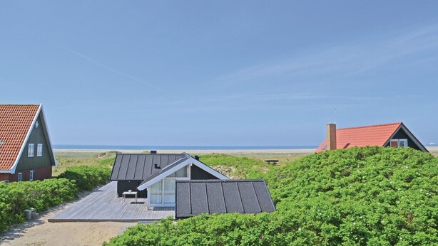 Une maison située sur la côte, dotée d’un toit en pente, d’une terrasse et offrant une vue sur la plage.