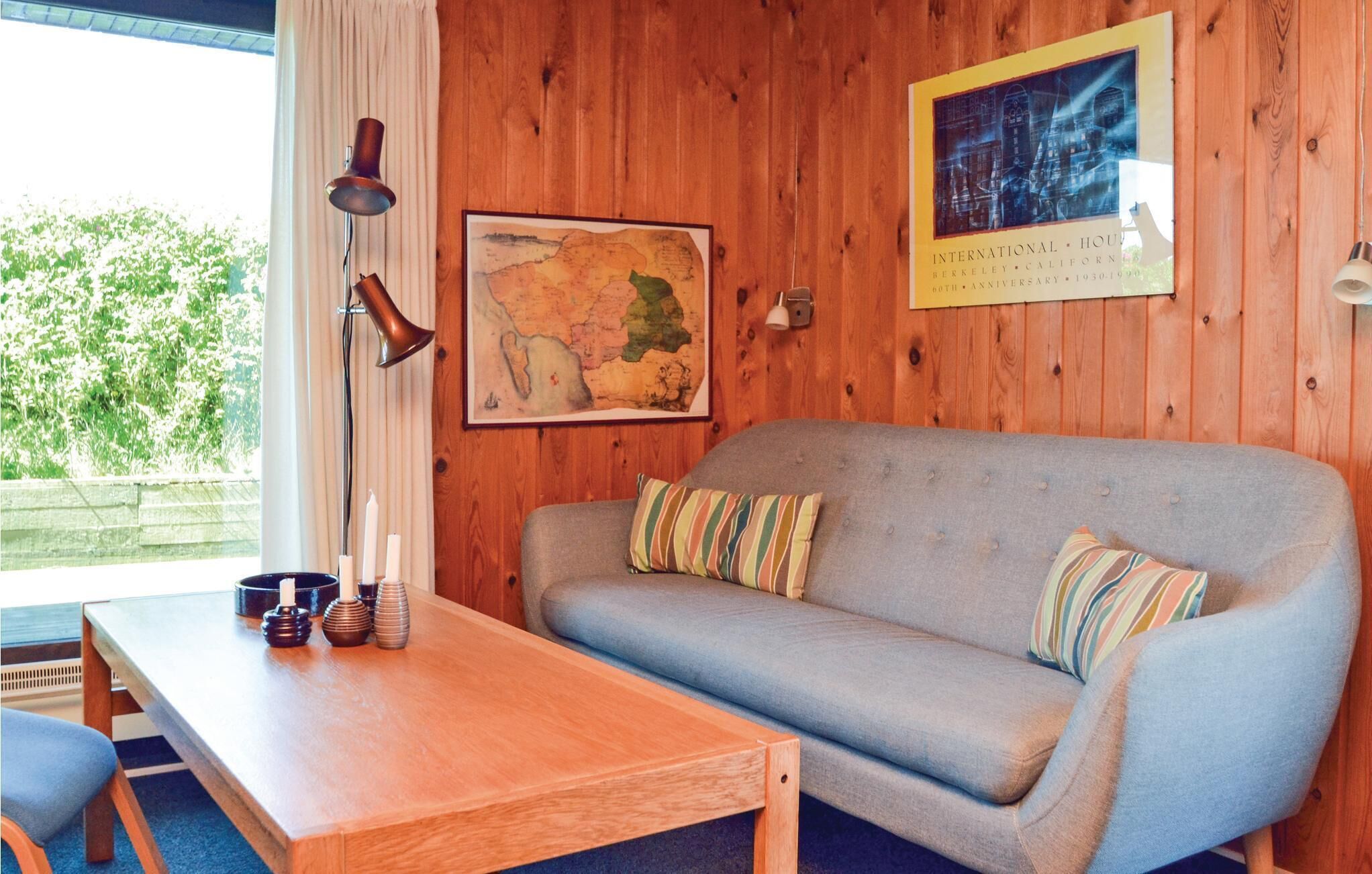 A room with a wooden wall, a grey sofa with striped pillows, a wooden table with candles, and a map and a framed picture on the wall.