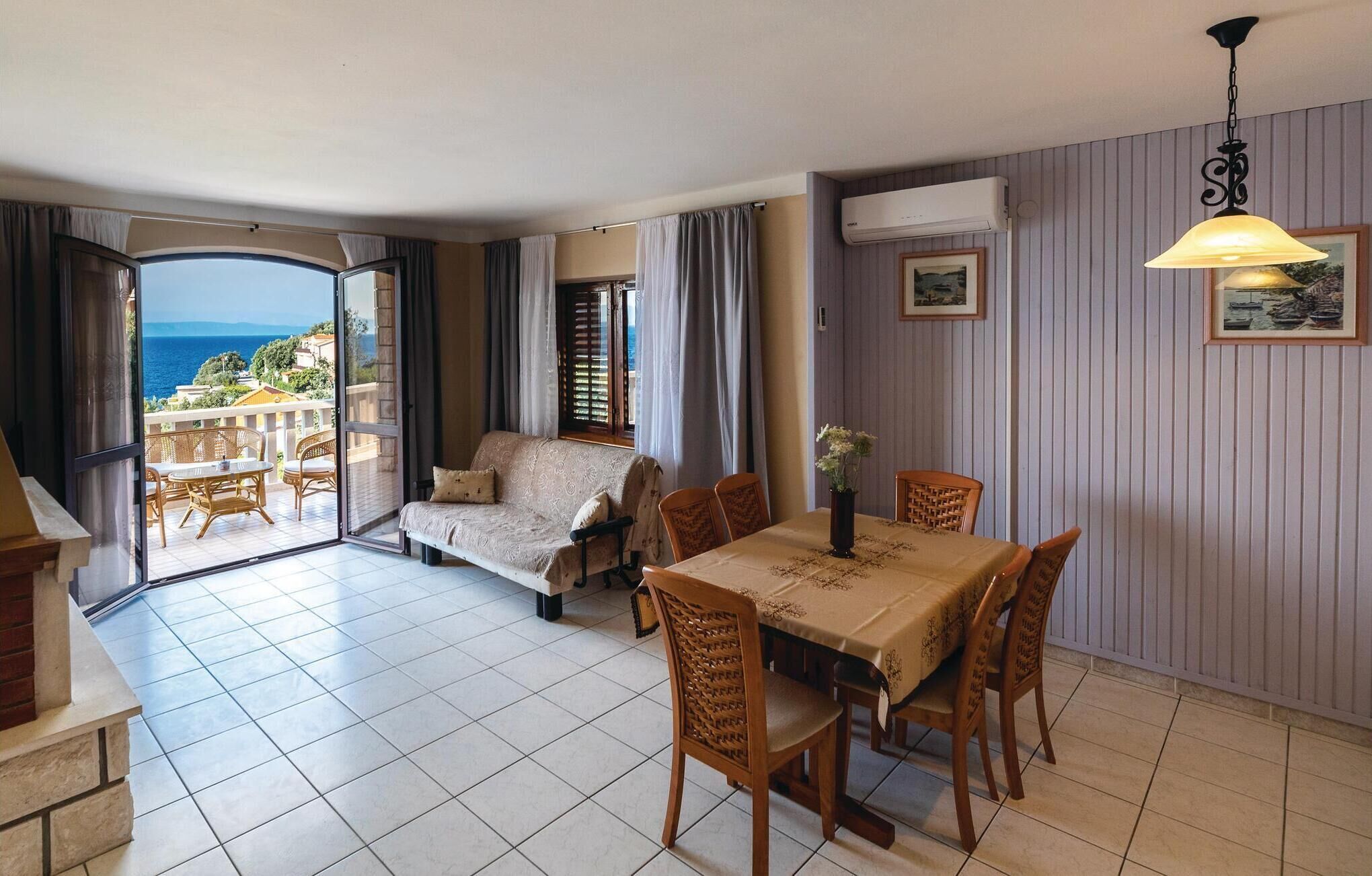 A dining area with a table and chairs, a sofa, and a view of the sea through a glass door.