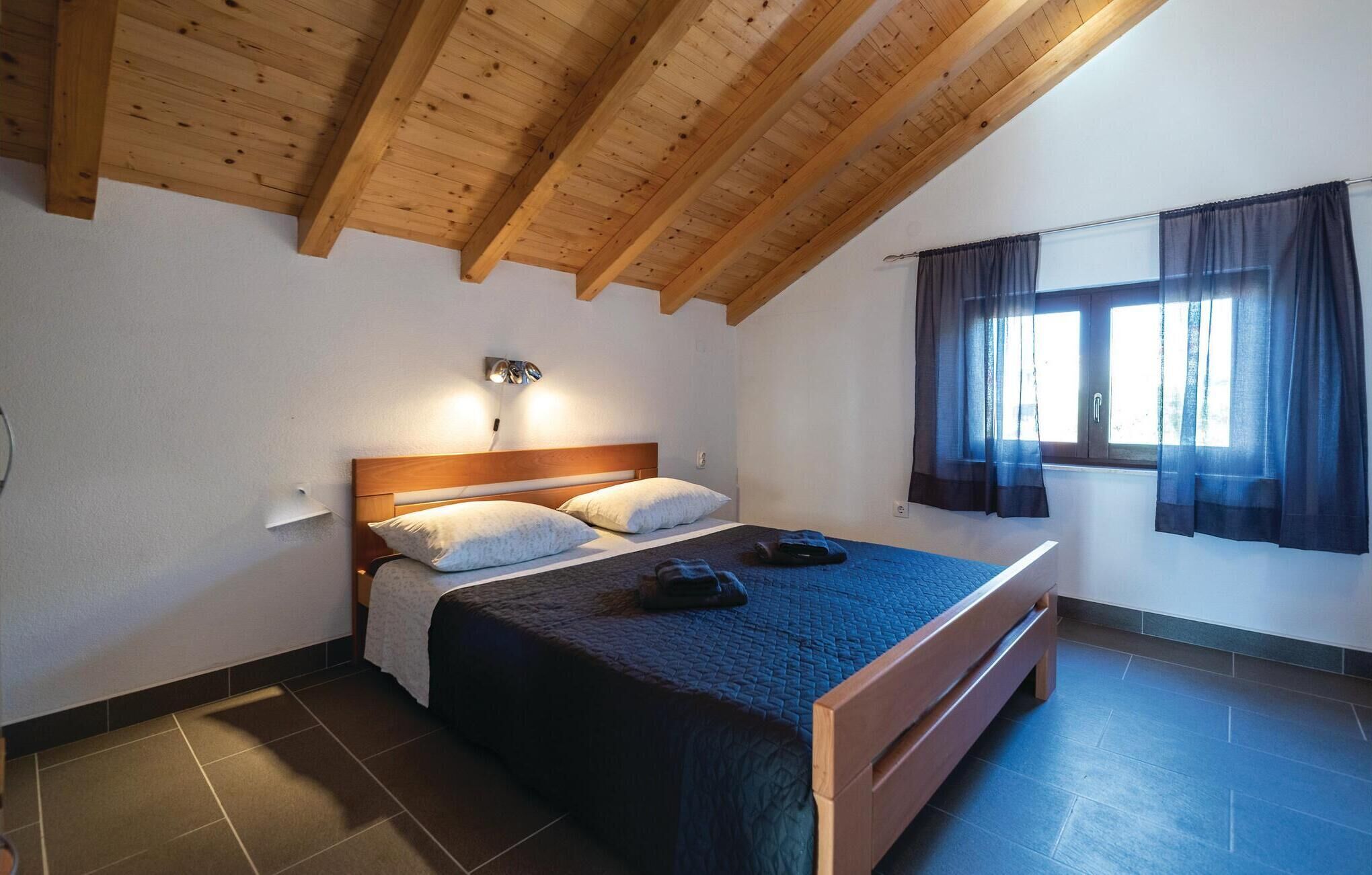 Un dormitorio con techo de madera, una cama con colcha azul y una ventana con cortinas.