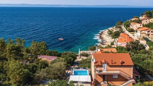 Vista sulla costa con mare cristallino, una barca e case dai tetti rossi.