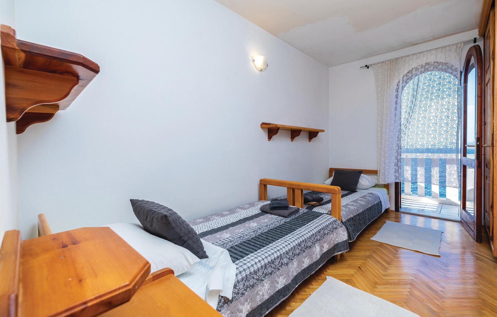 Een kleine kamer met twee bedden, een houten tafel, een klein plankje en een raam met uitzicht op het omliggende landschap.