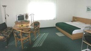 Ein Hotelzimmer mit Bett, Schreibtisch, Stuhl, Fernseher und einem Vorhangfenster.