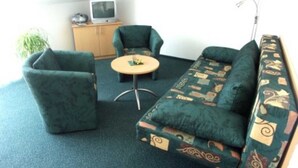 Ein kleiner, gemütlicher Raum mit einem grünen Sofa, zwei Sesseln, einem kleinen Tisch und einem Fernseher auf einem Schrank.