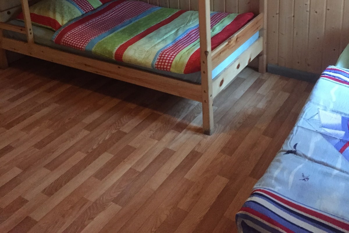 Kerrossänky värikkäillä vuodevaatteilla huoneessa, jossa on puuseinät ja -lattiat.