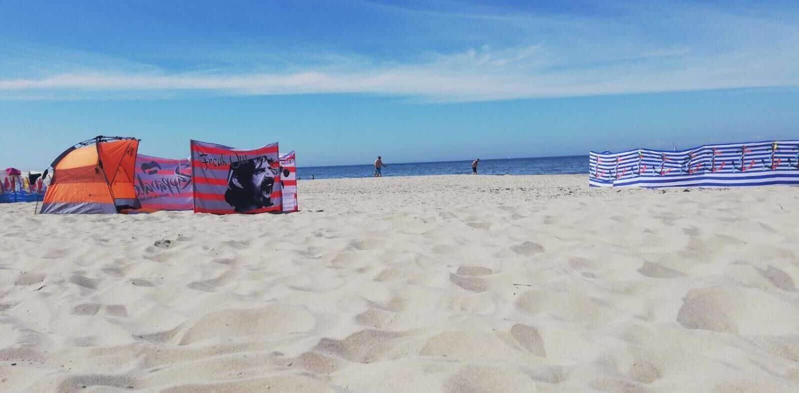 A sandy beach with tents and a striped beach umbrella.