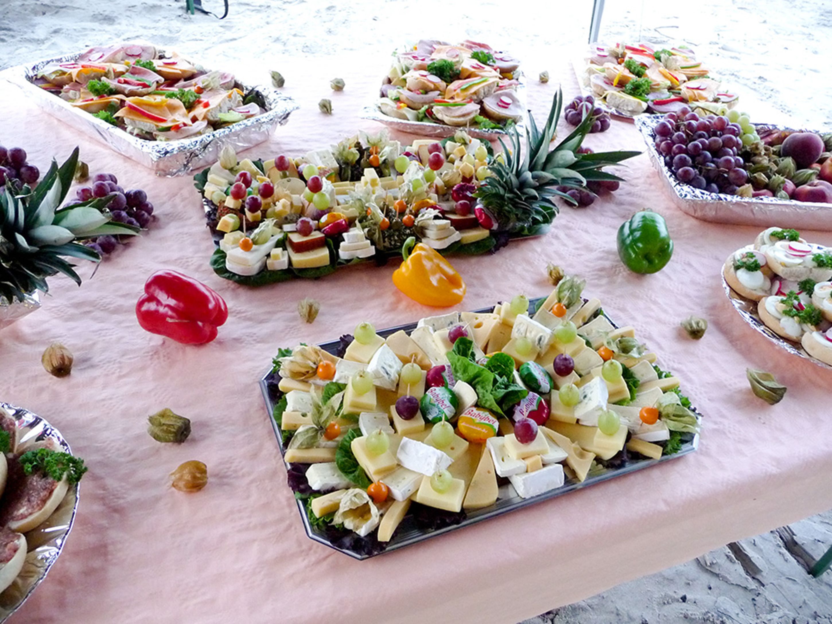 Una mesa con diferentes bandejas de comida que incluyen queso, frutas y verduras.