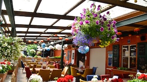 Un restaurante interior con vigas de madera, mesas, sillas y cestas de flores colgantes.