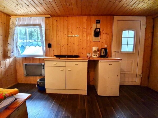 Una cocina compacta con paredes de madera, una ventana, microondas, cafetera y refrigerador.