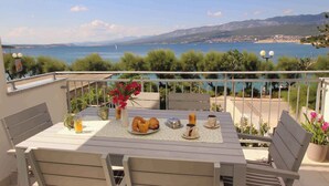 Ein Balkon mit Frühstückstisch, mit Blick auf die Küste und Berge in der Ferne.