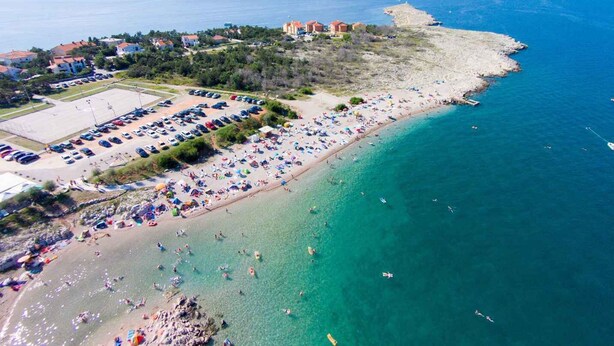 Luftaufnahme einer Küstenregion mit Strand, Parkplatz und Gebäuden.