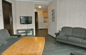 A living room with a wooden coffee table, two grey sofas, a TV on the wall, and a kitchen in the background. - Gorgeous apartment in Hemsedal (Hemsedal)