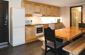 A compact kitchen with wooden cabinets, a white refrigerator, a microwave, an oven, and a coffee maker. There is a wooden dining table with a bench and a chair. - Gorgeous apartment in Hemsedal (Hemsedal)