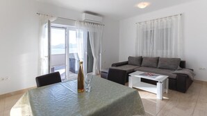 Ein Wohnzimmer mit einer Couch, einem Couchtisch und einem Esstisch. Auf dem Esstisch steht eine Weinflasche.