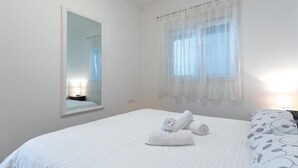 Ein Hotelzimmer mit Bett, Spiegel, Fenster mit leichtem Vorhang und Nachttischlampe.