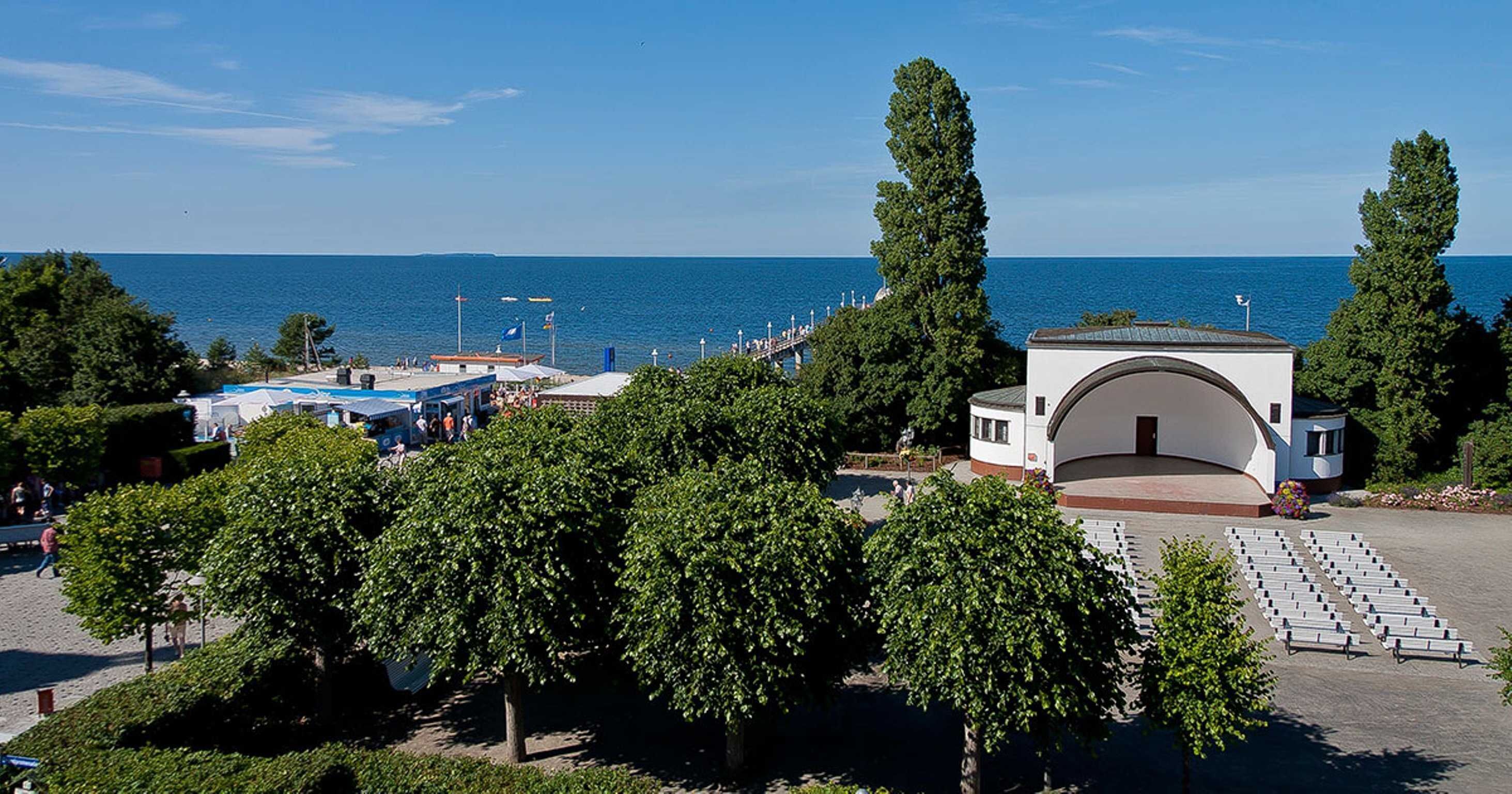 Eine Küstenlandschaft mit einem großen weißen Gebäude, Bäumen und Blick auf das Meer.