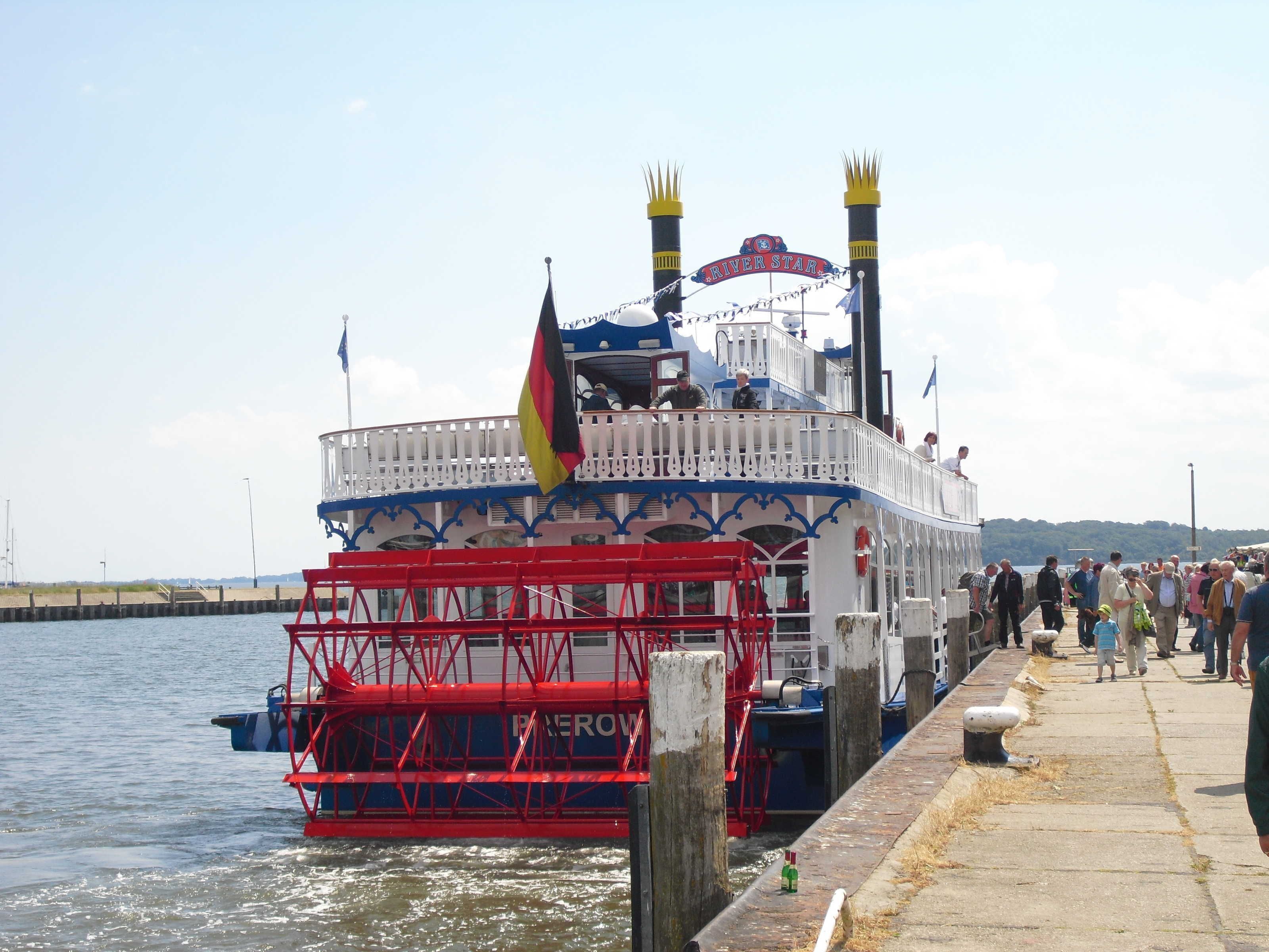 A riverboat docked at a pier with a crowd of people on the dock.