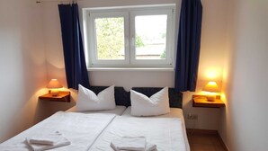 A double bed with white linens, two pillows, and a window with curtains.