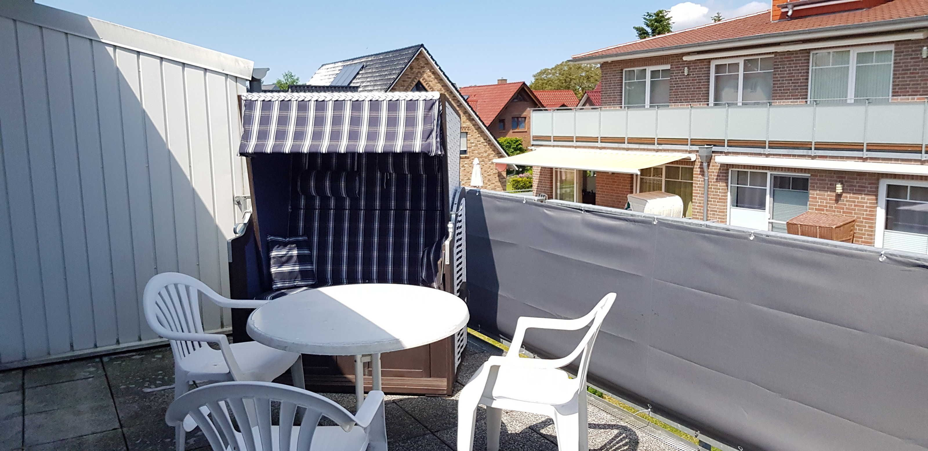 A small outdoor seating area with a table and two chairs, a covered seating area with a striped awning, and a grey wall.