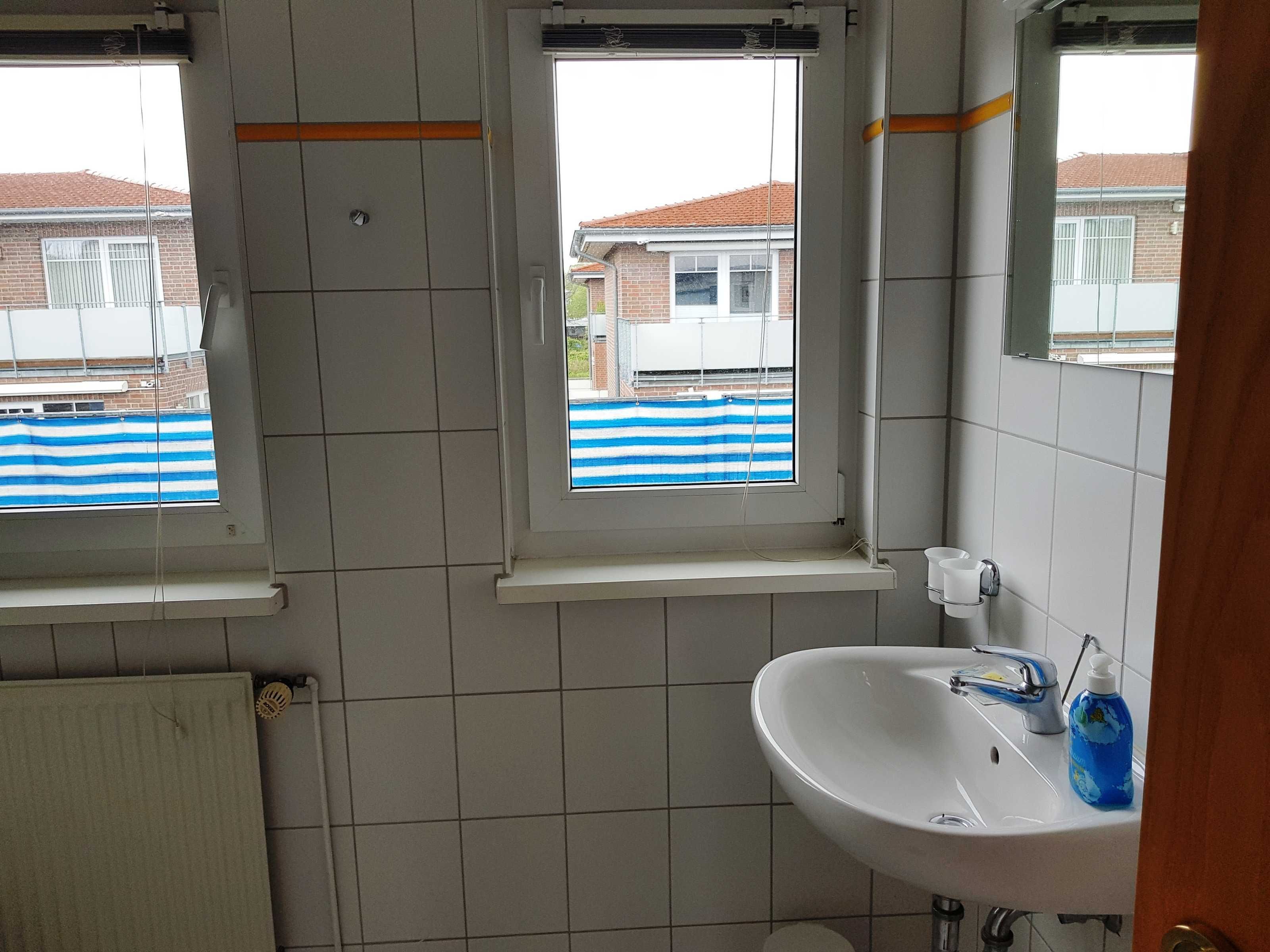 A bathroom with a white sink, a window with a blue and white striped blind, and a tiled wall.