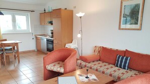 A living room with a sofa, a dining table, and a kitchen area with cabinets and appliances.