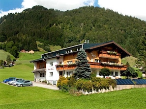 A two-story building with a sloped roof, a balcony with plants, and solar panels on the roof.